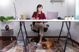 Asian woman working on her work desk as her dog rests under it