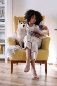 A woman sitting on a yellow couch with a dog.
